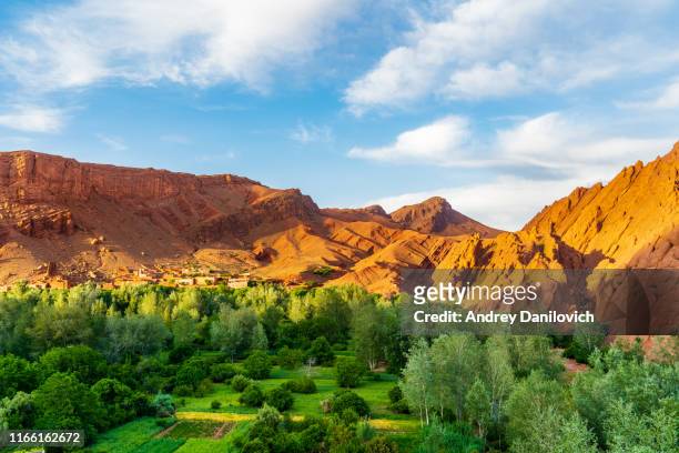 red moroccan atlas mountains, and valley with green trees. blue cloudy sky on the background. - atlas maroc stock pictures, royalty-free photos & images