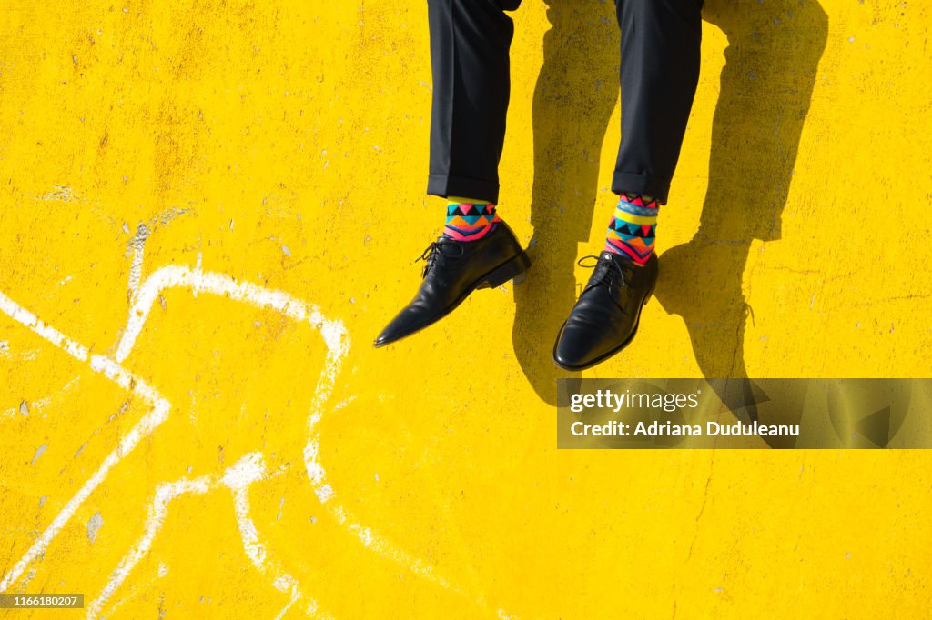 Section basse d’un homme portant des chaussures assis sur un mur jaune