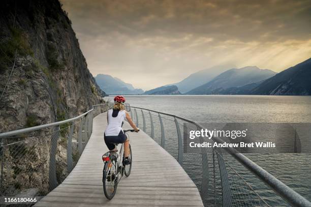 female tour cyclist rides a modern cycle path around lake garda - pista ciclabile foto e immagini stock