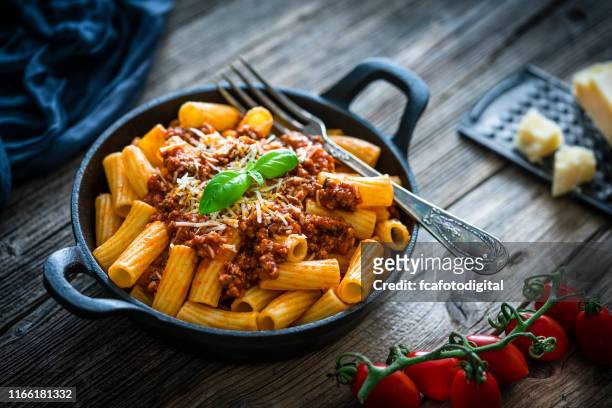 rigatoni pasta with bolognese sauce shot on rustic wooden table - bolognese sauce stock pictures, royalty-free photos & images