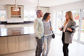 Female Real Estate Agent Showing Couple Interested In Buying Around House