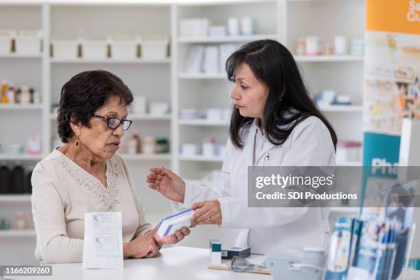 senior woman holds medication box as pharmacist talks - pharmacist and patient stock pictures, royalty-free photos & images