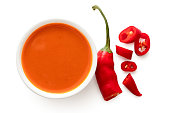 Peri peri chilli sauce in a white ceramic bowl next to a cut up chilli pepper isolated on white from above.