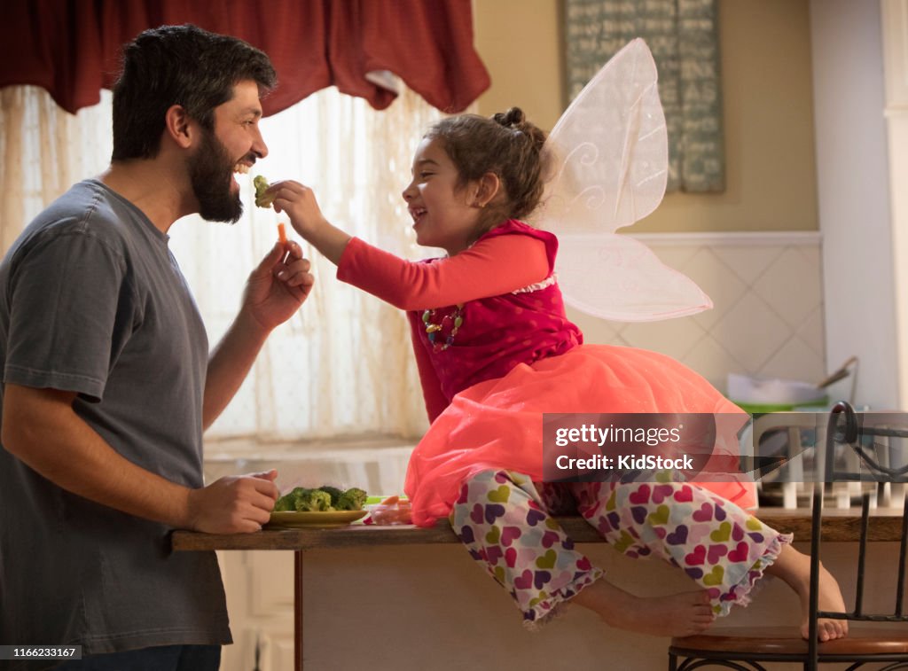 Smiling little girl feeding her father with a broccoli