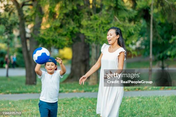 mutter und sohn spielen fußball im öffentlichen park - soccer mum stock-fotos und bilder