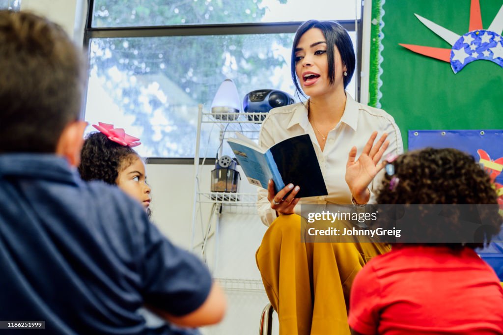 Hispanic schoolteacher reading aloud to her young students