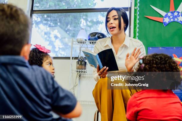 hispanic schoolteacher reading aloud to her young students - preschool classroom stock pictures, royalty-free photos & images