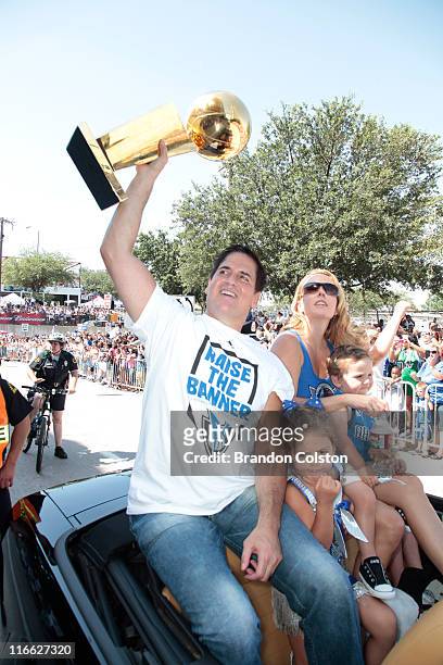 Mark Cuban, owner of the Dallas Mavericks hoists the Larry O'Brien trophy above his head as he and his family ride along during the Mavericks NBA...