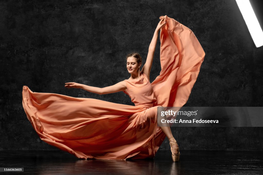 Ballerina. A young ballet dancer dressed in a long peach dress, pointe shoes with ribbons. The girl performs an elegant, graceful dance movement. Beautiful classic ballet. Advertising ballet studio.