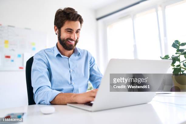 smiling businessman with headphones sitting at a desk using a laptop - gifted movie stock-fotos und bilder