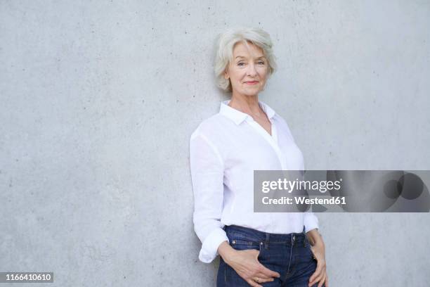 portrait of relaxed mature woman wearing white shirt leaning against concrete wall - hair woman mature grey hair beauty stockfoto's en -beelden