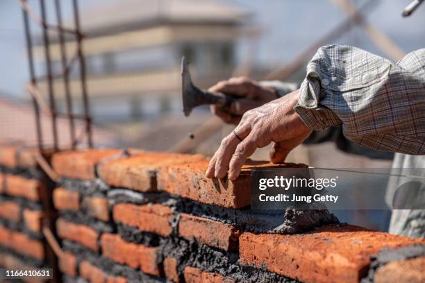 bricklayer industrial worker installing brick masonry with trowel putty knife at construction site - ouvrier maçon photos et images de collection