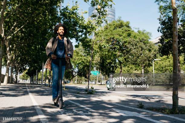 man with backpack riding his e-scooter on a bicycle lane - single lane road - fotografias e filmes do acervo