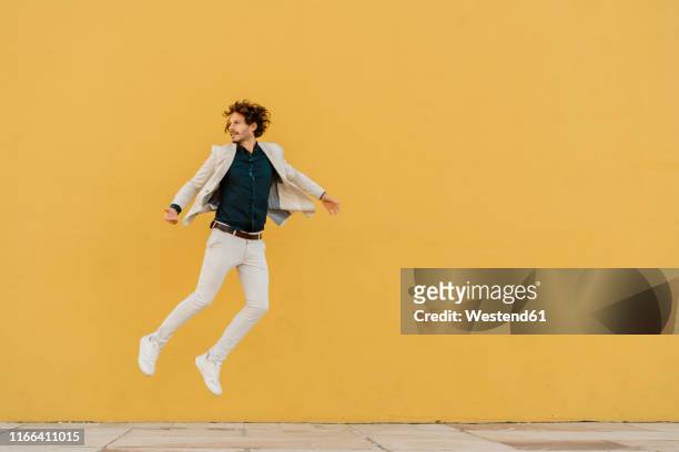 businessman jumping in the air in front of yellow wall - floating fotografías e imágenes de stock