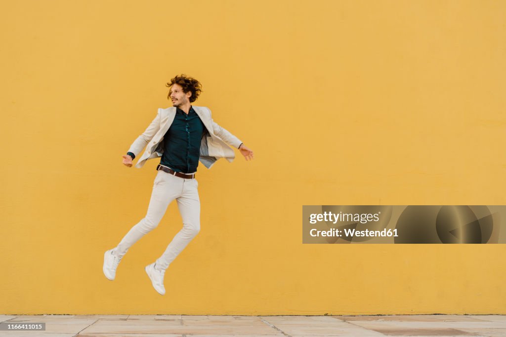 Businessman jumping in the air in front of yellow wall