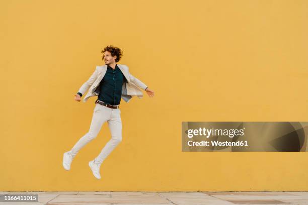 businessman jumping in the air in front of yellow wall - up in the air stock pictures, royalty-free photos & images