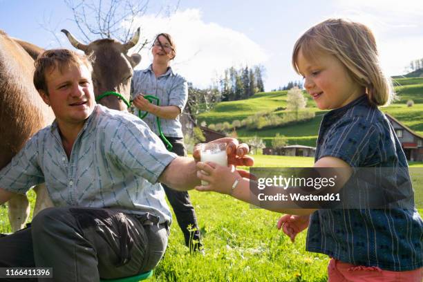 farmer giving his daughter a glass of fresh milk from a cow on pasture - milk family stockfoto's en -beelden