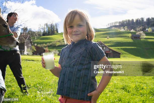 portrait of smiling girl holding a glass of fresh milk on pasture - farmer cow stock-fotos und bilder