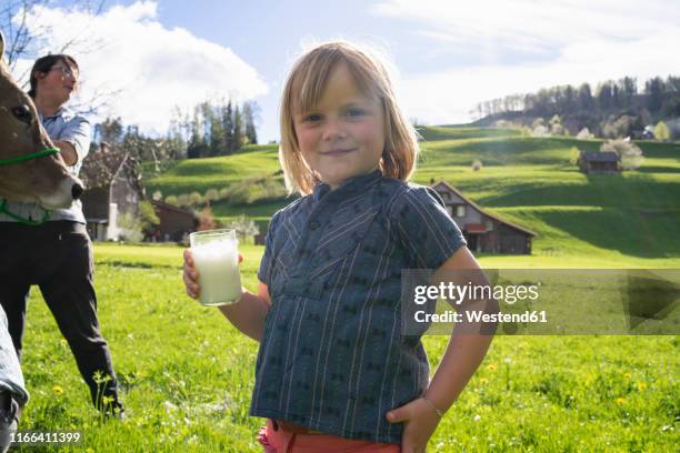 portrait of smiling girl holding a glass of fresh milk on pasture - swiss cow stock pictures, royalty-free photos & images