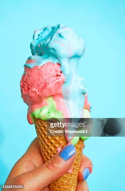 woman's hand holding ice-cream cone with melting icecream in front of blue background - multi coloured hands stock pictures, royalty-free photos & images