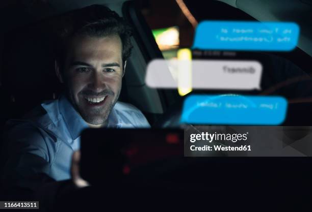 smiling businessman using cell phone for messaging i in car at night - fachmann auto smartphone stock-fotos und bilder