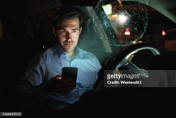 businessman using smartphone in car at night surrounded by virtual shining globe - fachmann auto smartphone stock-fotos und bilder