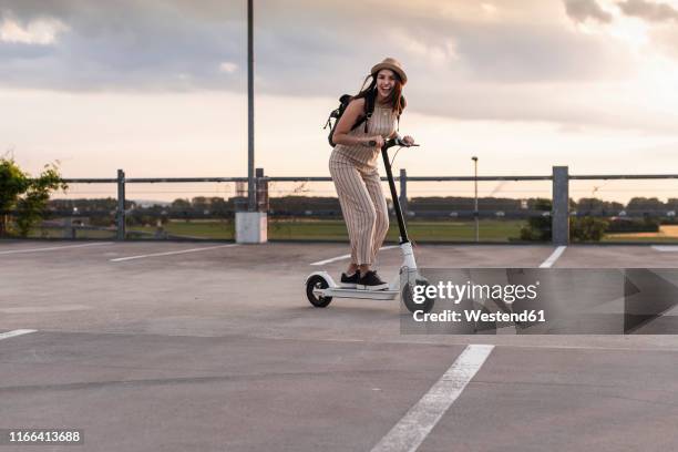 happy young woman on electric scooter on parking deck - mobility scooters stockfoto's en -beelden