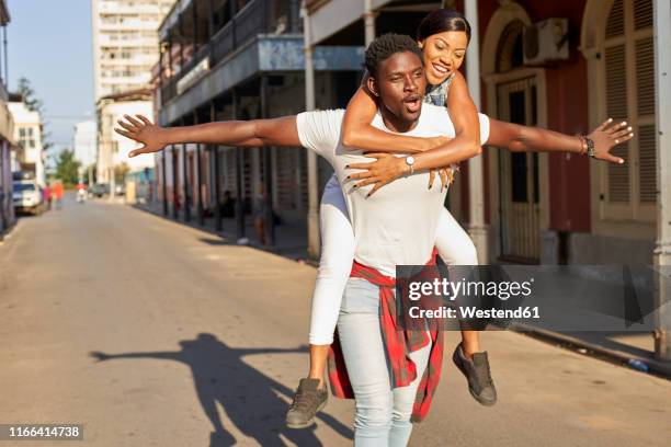 young man carrying girlfriend piggyback in the street, mabuto, mozambique - 飛行機のまね ストックフォトと画像