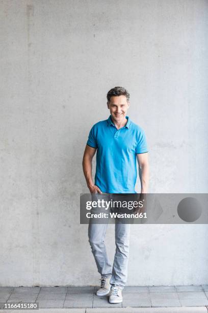 mature man wearing blue poloshirt, grey wall in the background - blue polo shirt photos et images de collection