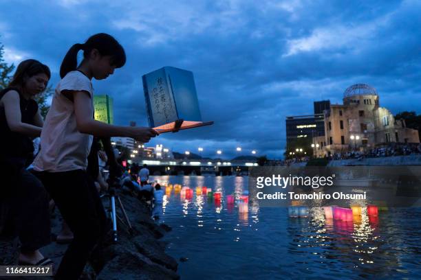 Woman places a candle lit paper lantern on the river during an event to commemorate the 74th anniversary of the atomic bombing of Hiroshima at the...