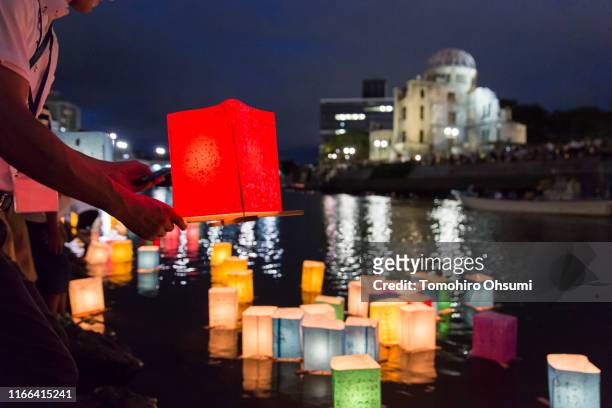Man prepares to float a candle lit paper lantern on the river during an event to commemorate the 74th anniversary of the atomic bombing of Hiroshima...