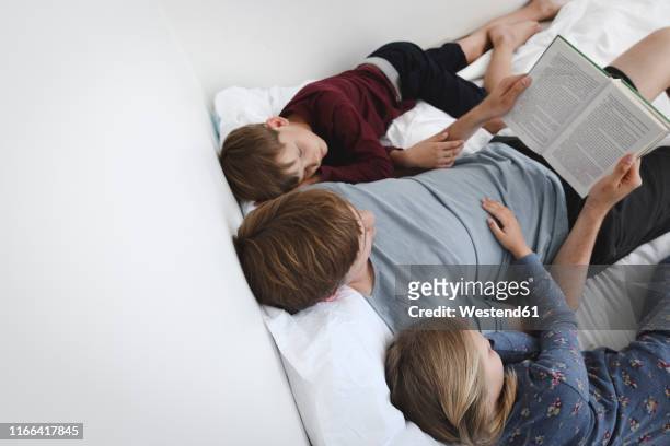 father reading book with daughter and son in bed - bedtime story book stock pictures, royalty-free photos & images