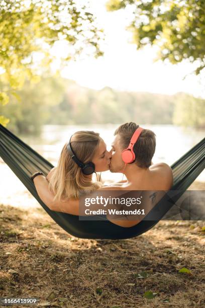 couple relaxing in hammock by the lake, kissing, listening music - young man listening music and relaxing in hammock stock pictures, royalty-free photos & images