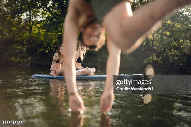 young man diving into lake, young women on paddleboard warching - woman jumping lake bildbanksfoton och bilder