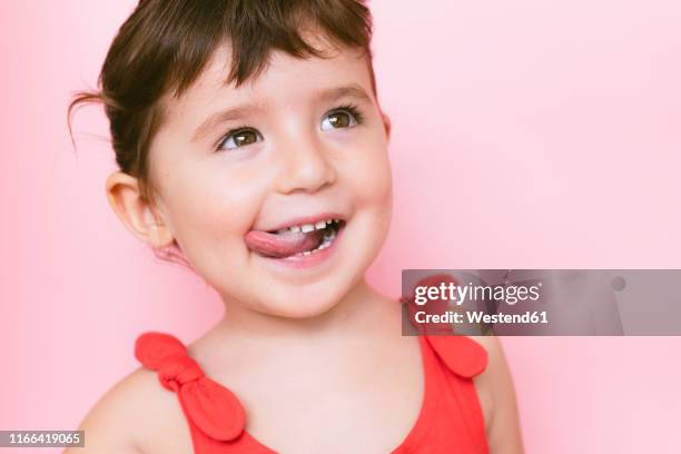 portrait of little girl sticking out tongue in front of pink background - 3 years brunette female alone caucasian stock pictures, royalty-free photos & images