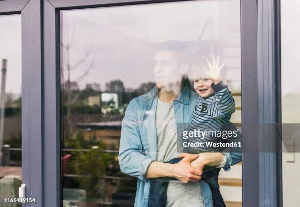 father holding laughing son, looking out of window - fenster stock-fotos und bilder