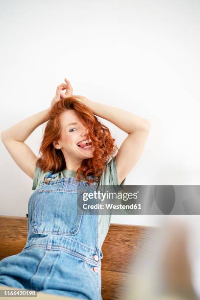 portrait of laughing redheaded woman wearing dungarees sticking out tongue - peto prenda de vestir fotografías e imágenes de stock