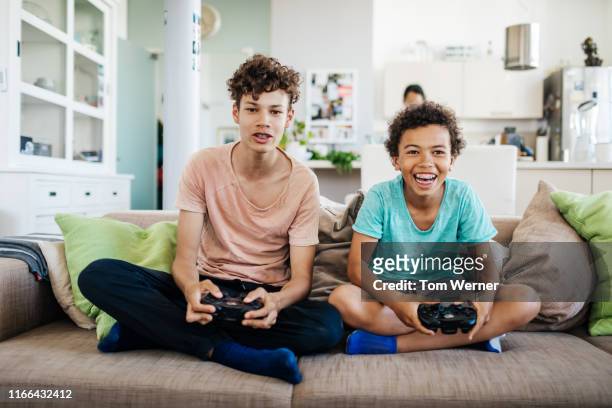 two brothers sitting on couch playing computer games - sibling stock photos et images de collection