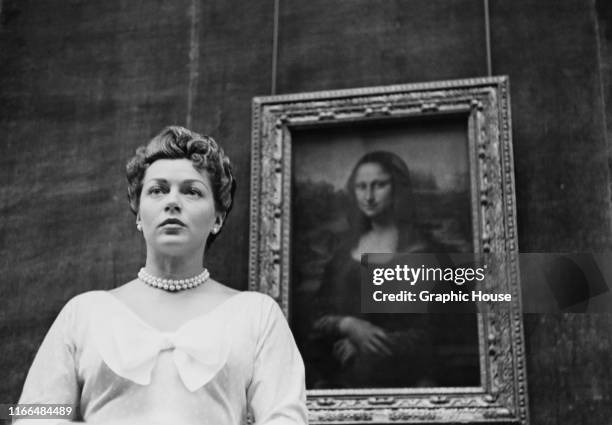 American actress Lana Turner stands in front of the 'Mona Lisa' by Leonardo da Vinci during a visit to the Louvre in Paris, France, 1953.