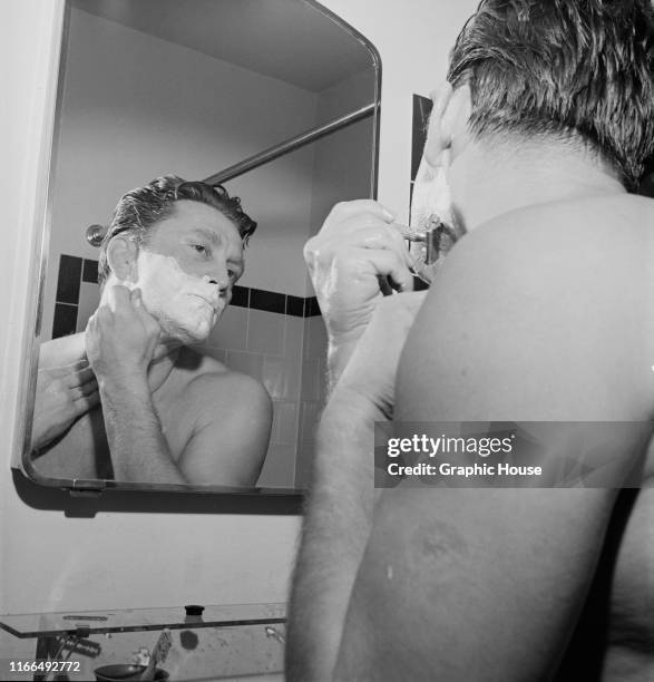 American actor Kirk Douglas shaves in front of a mirror in the morning, 1952.