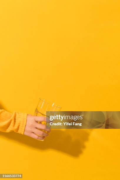 hand holding empty glass in front of yellow background - empty glass stock pictures, royalty-free photos & images