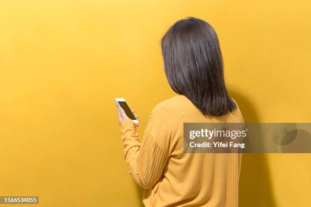 woman in yellow looking at cell phone in front of yellow background - woman front and back stockfoto's en -beelden