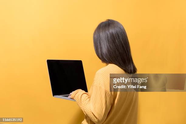 woman in yellow holding laptop in front of yellow background - woman laptop screen stockfoto's en -beelden