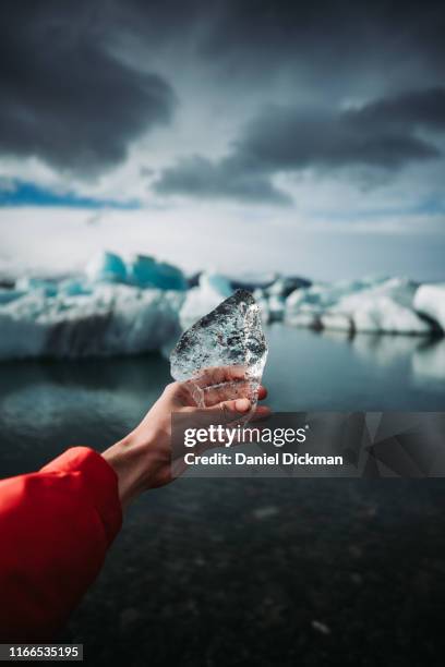 holding an ice shard at a glacier lagoon in iceland - jokulsarlon lagoon stock pictures, royalty-free photos & images