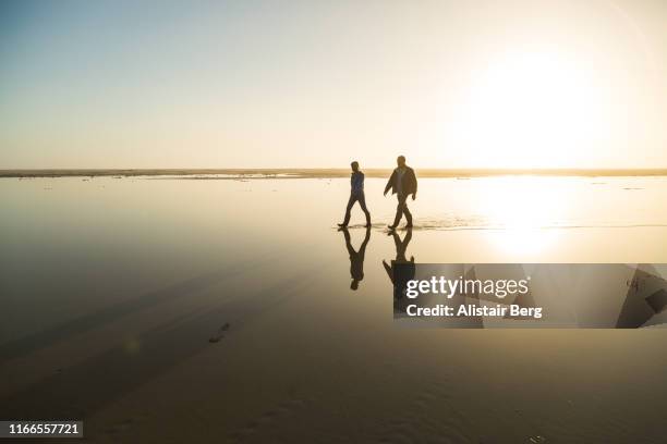 couple walking through beach lagoon at sunset - sunset silhouette back lit stock pictures, royalty-free photos & images