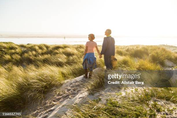 senior couple walking through sand dunes by the beach - romantic picnic stockfoto's en -beelden