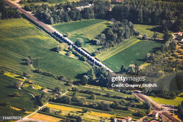 aerial view on freight train railroad track crossing in diagonal the french countryside in summer, in middle of vibrant green fields from ain department, auvergne-rhone-alpes region - train france stock pictures, royalty-free photos & images