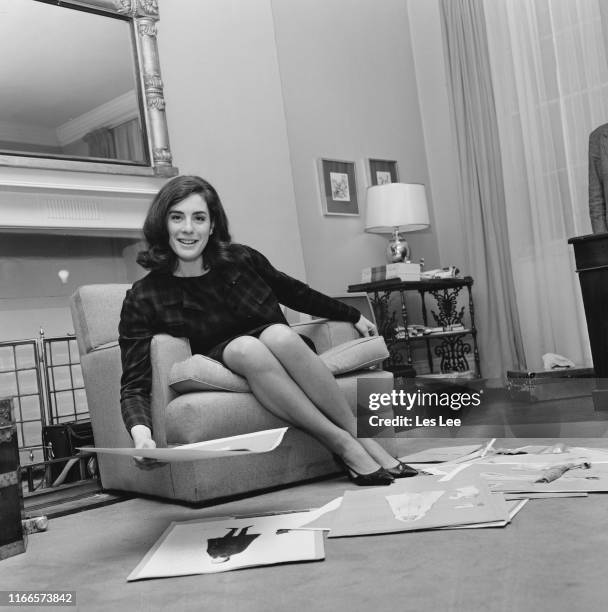 English actress and author Eleanor Bron looking at outfits designs in a living room, UK, 8th February 1965.