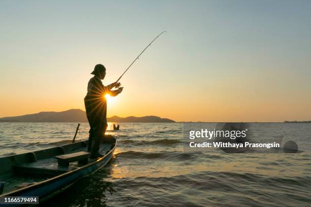 young man fishing on a lake from the boat at sunset - freshwater fishing stock photos et images de collection