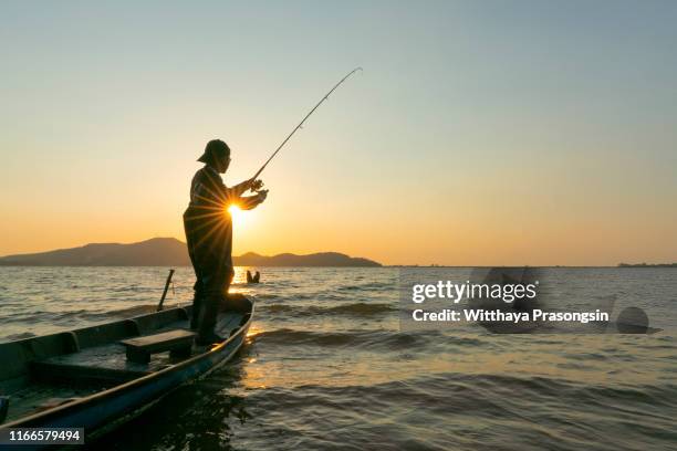 young man fishing on a lake from the boat at sunset - rod stock pictures, royalty-free photos & images